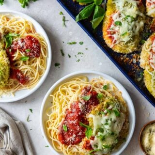 Baked chicken pesto parmesan served on plates over spaghetti.