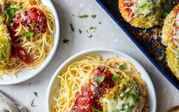 Baked chicken pesto parmesan served on plates over spaghetti.