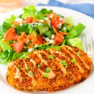 A crispy buffalo chicken breast on a plate next to a green side salad.