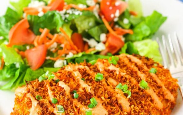 A crispy buffalo chicken breast on a plate next to a green side salad.