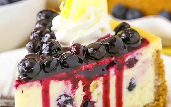 A slice of lemon blueberry cheesecake piled high with blueberry topping and whipped cream.