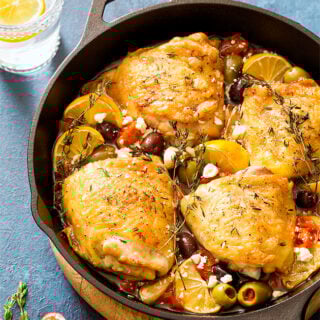 Mediterranean roasted chicken thighs in a skillet with tomatoes, olives, and feta cheese.