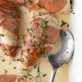 Prosciutto wrapped chicken in a creamy sauce, next to a spoon.