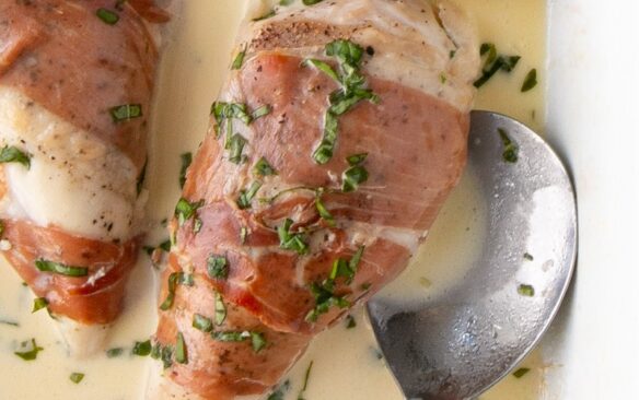 Prosciutto wrapped chicken in a creamy sauce, next to a spoon.