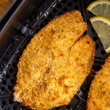 crispy tilapia in air fryer basket with parsley and lemon slices