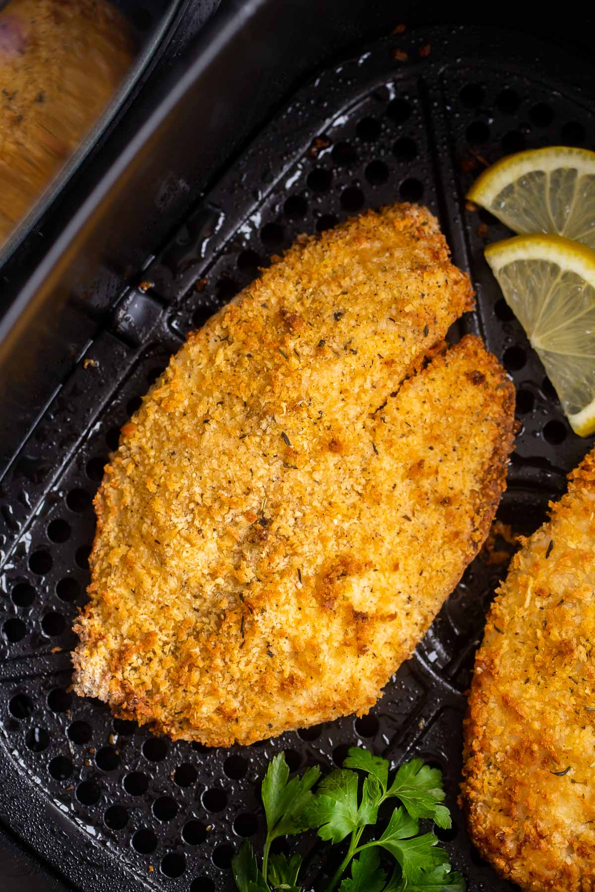 crispy tilapia in air fryer basket with parsley and lemon slices