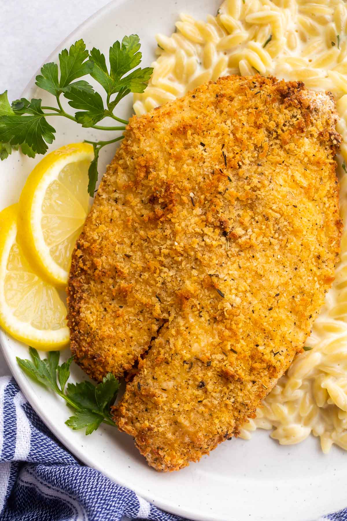 close up image of air fryer tilapia with lemon slices and parsley sprigs