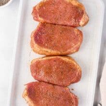 overhead image of uncooked pork chops on sheet pan well seasoned