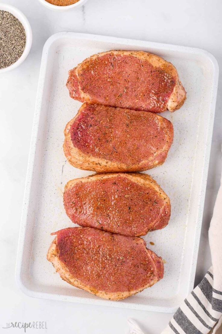 overhead image of uncooked pork chops on sheet pan well seasoned