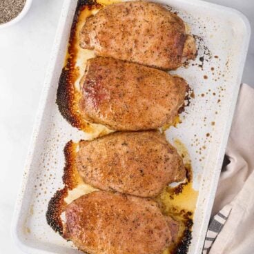 square image of baked pork chops in a white pan.