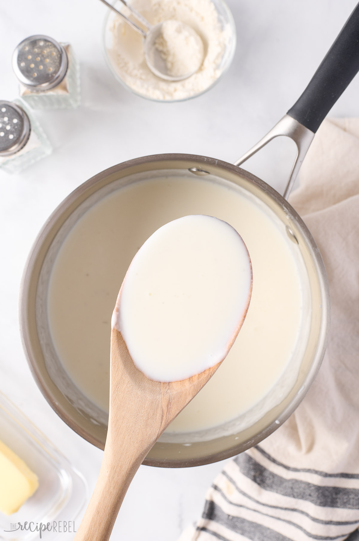 wooden spoon scooping bechamel sauce out of pot