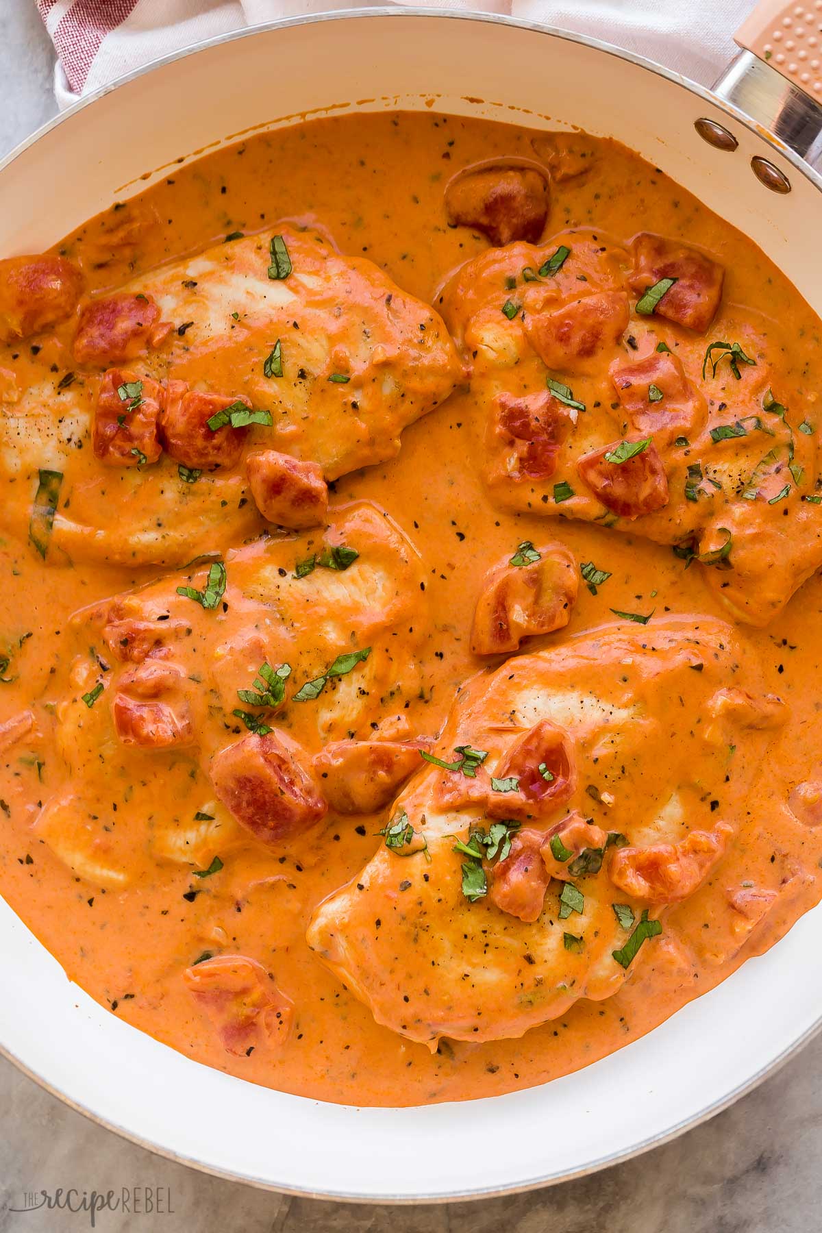 close up overhead image of tomato basil chicken breasts in white skillet