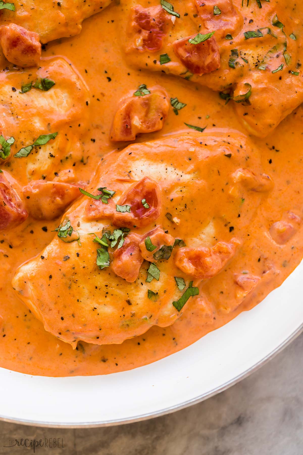 close up image of single chicken breast in creamy tomato basil sauce with parsley on top