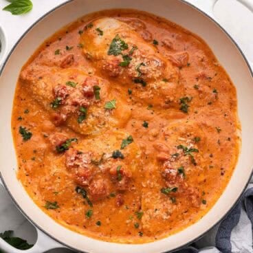 square image of four chicken breasts in tomato basil sauce in a white skillet.