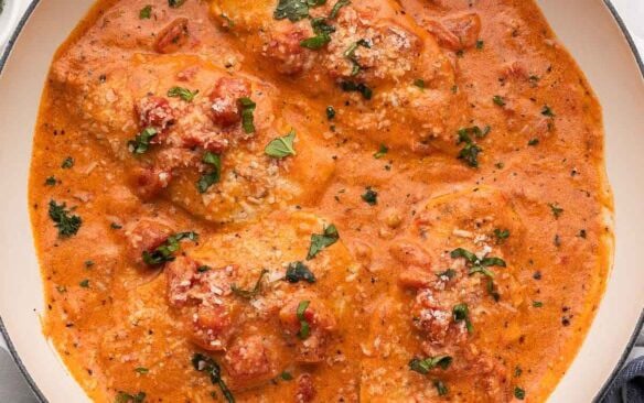 square image of four chicken breasts in tomato basil sauce in a white skillet.