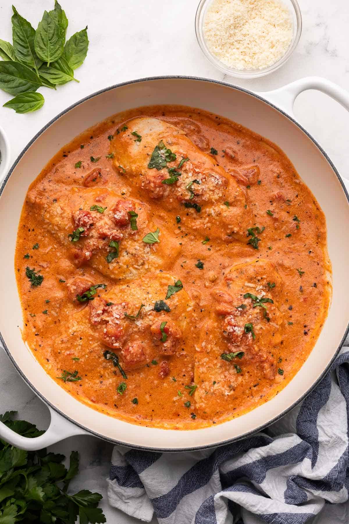 overhead image of creamy tomato basil chicken breasts in a white braiser.
