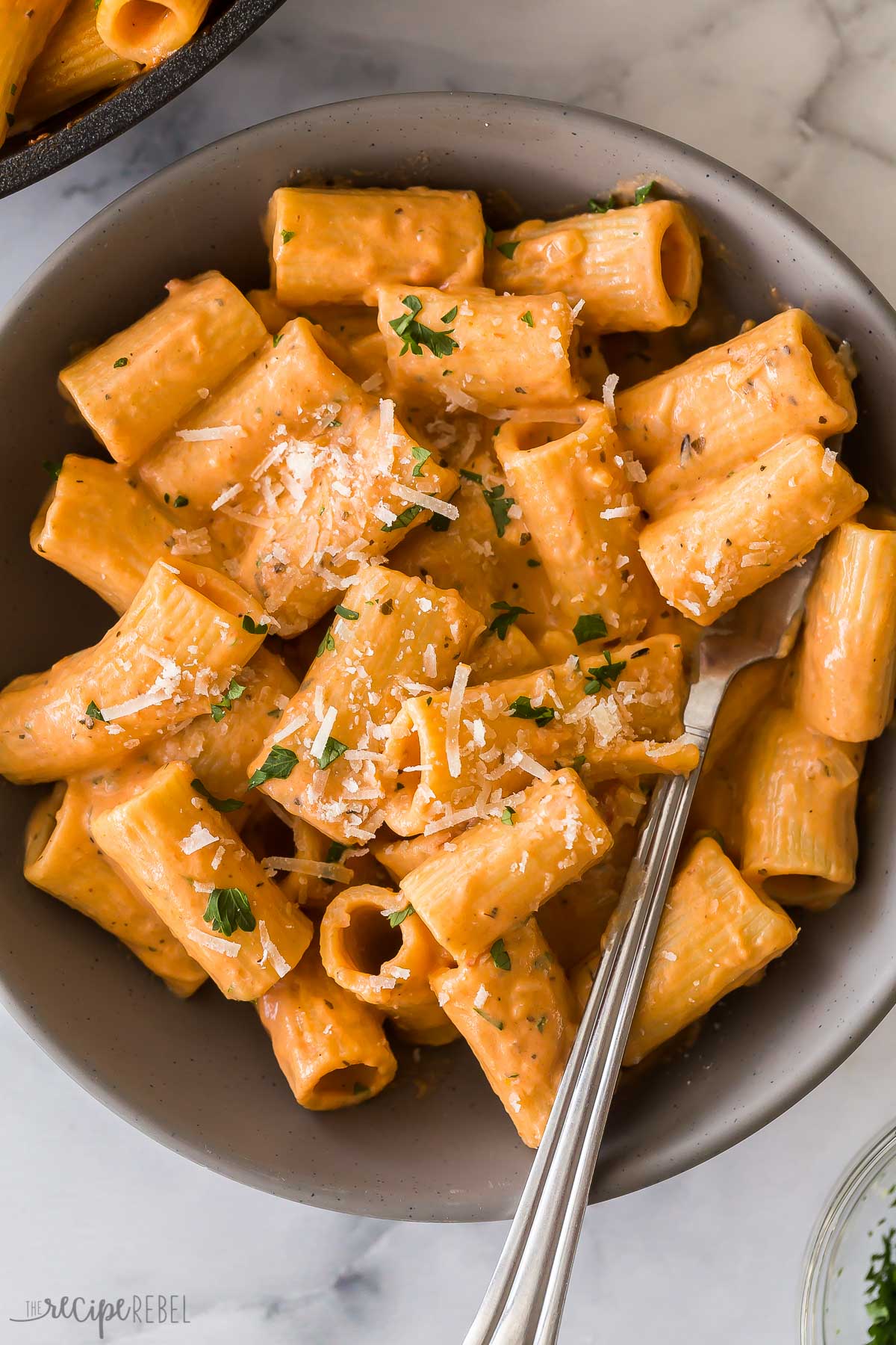 This Creamy Tomato Rigatoni Pasta is the perfect easy weeknight dinner! It's a 25-minute recipe made with tender rigatoni pasta that are tossed in a rich, creamy, and flavorful tomato sauce and finished off with a sprinkle of parmesan. #rigatoni #dinner | easy dinner ideas | 30 minute meals | easy recipes | pasta | rigatoni pasta | comfort food rigatoni pasta in creamy tomato sauce in grey bowl