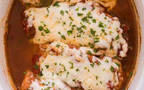overhead image of four salsa chicken breasts in slow cooker with mozzarella and parsley