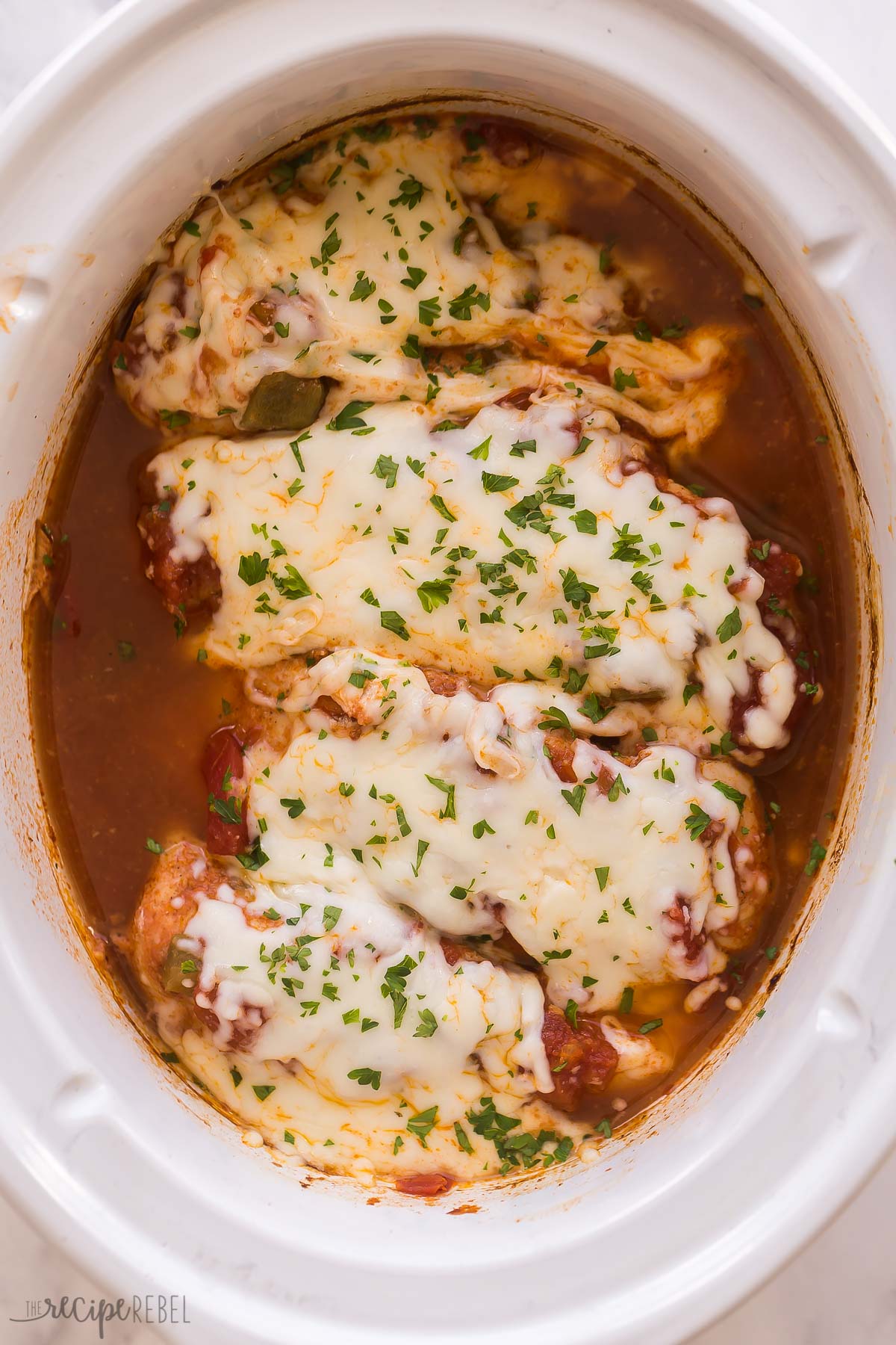 overhead image of four salsa chicken breasts in slow cooker with mozzarella and parsley