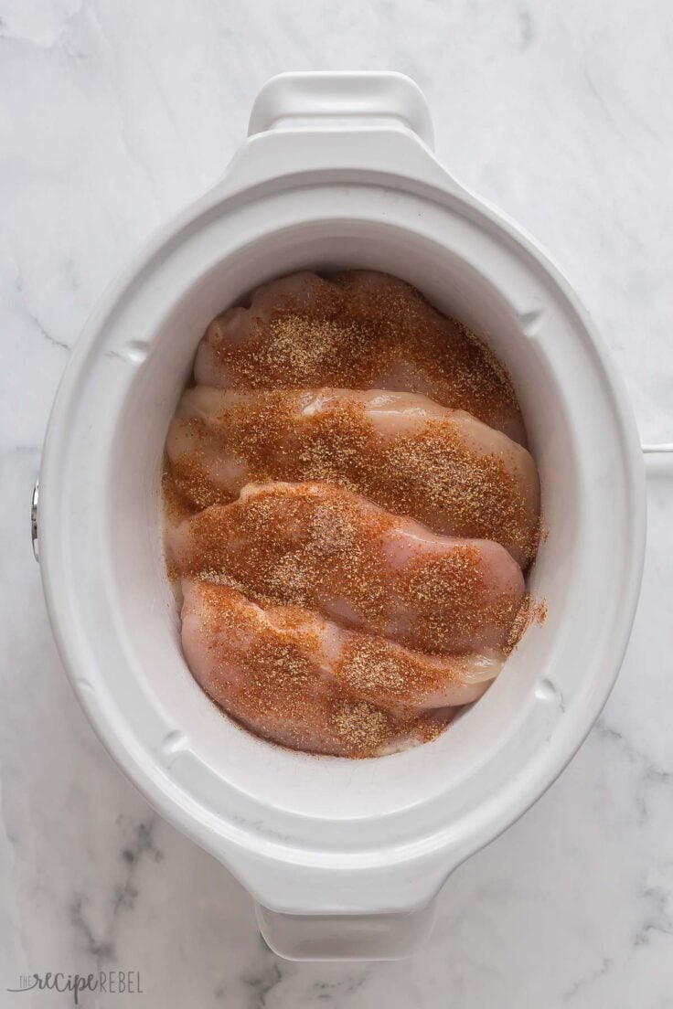 seasoning sprinkled over uncooked chicken breasts in slow cooker