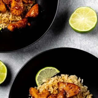 Honey lime chicken served over rice on black plates.