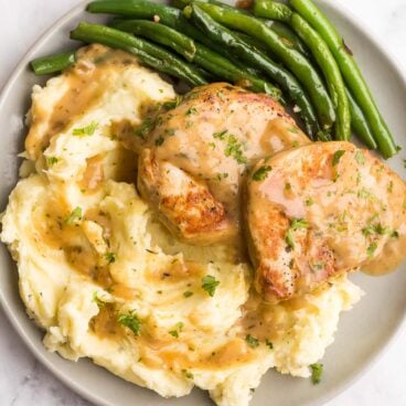 overhead image of two boneless pork chops with gravy over mashed potatoes with green beans