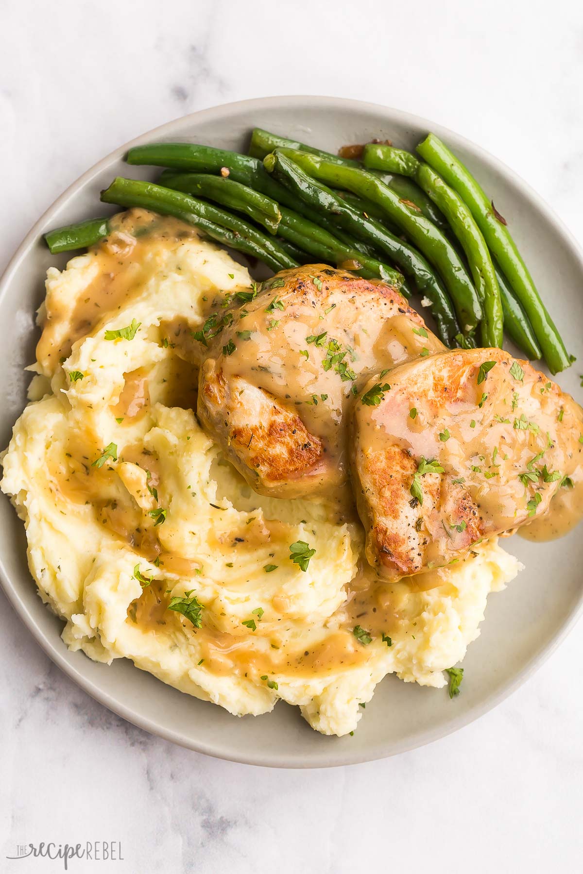 overhead image of two boneless pork chops with gravy over mashed potatoes with green beans