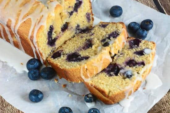 A loaf of lemon blueberry pound cake sliced to reveal insides filled with fresh blueberries.