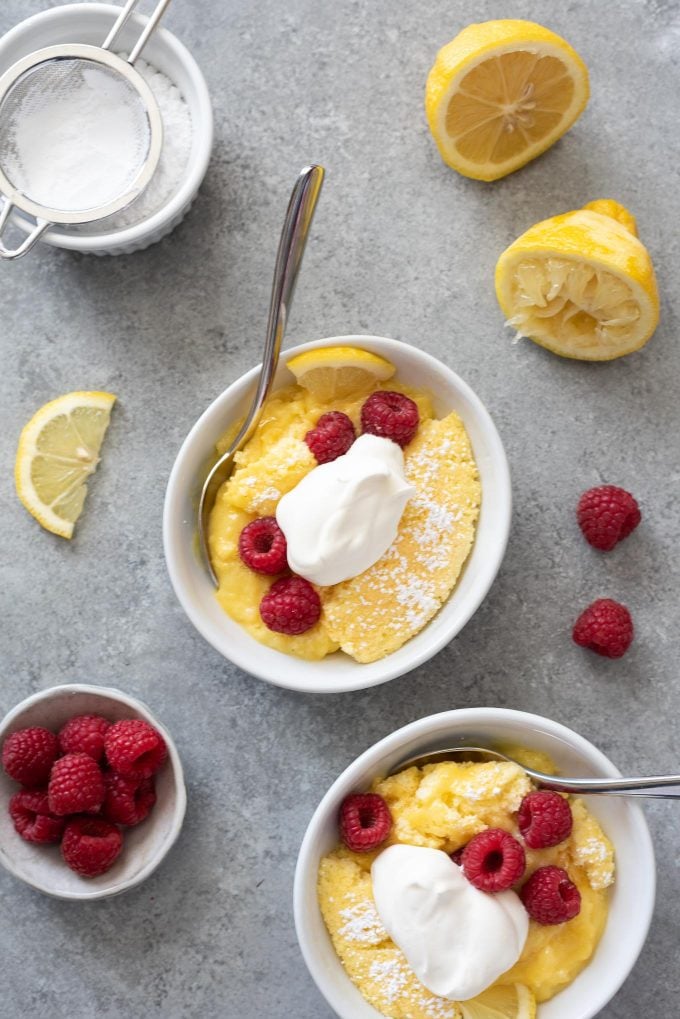 Bowls of lemon pudding cake topped with berries and whipped cream.