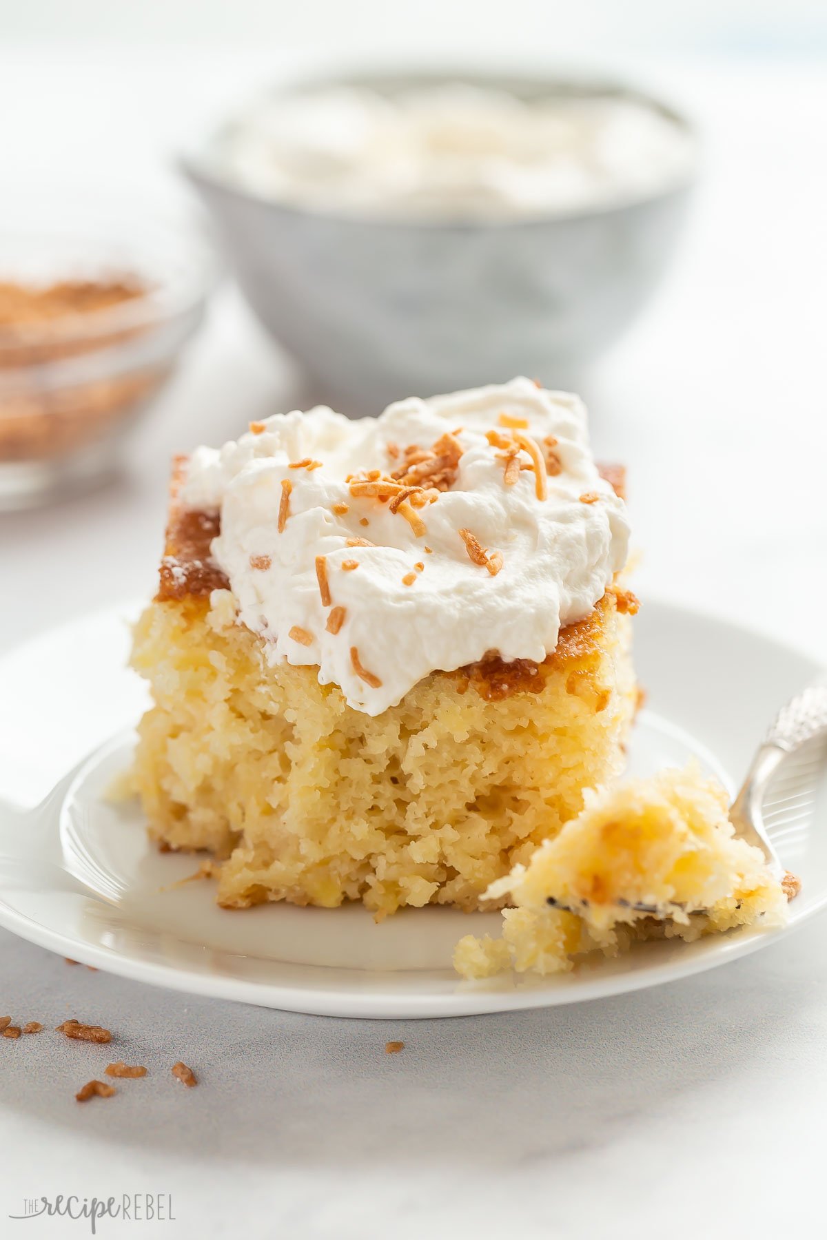 piece of pineapple cake on white plate with whipped cream and toasted coconut