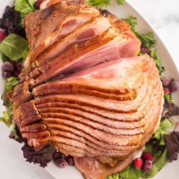 glazed spiral ham on a white platter with greens'