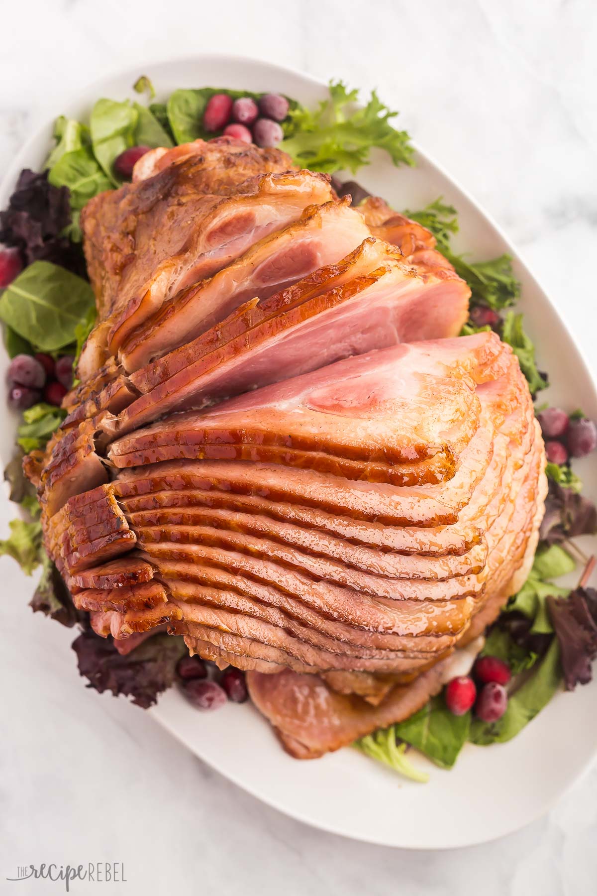 glazed spiral ham on a white platter with greens'