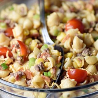 Cowboy pasta salad in a clear bowl with a silver serving spoon.