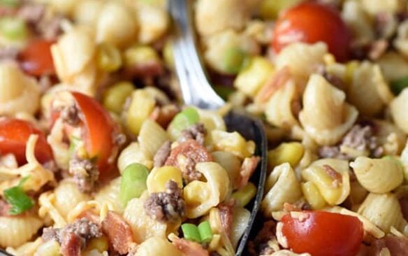 Cowboy pasta salad in a clear bowl with a silver serving spoon.
