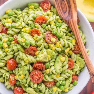 Creamy avocado pasta salad served in a large white bowl with a wooden spoon.