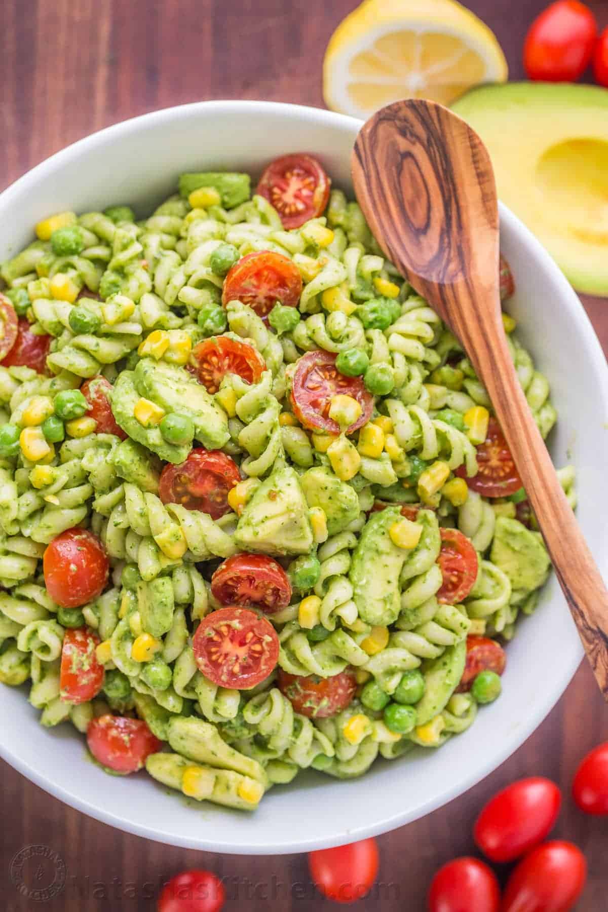 Creamy avocado pasta salad served in a large white bowl with a wooden spoon.