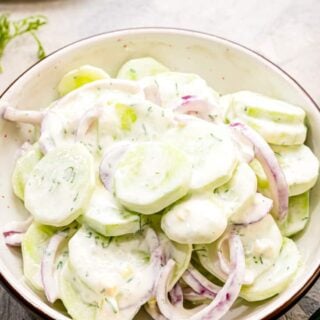 A bowl of creamy cucumber salad with red onions.