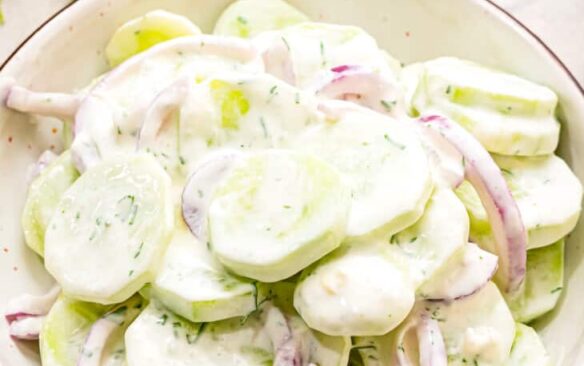A bowl of creamy cucumber salad with red onions.