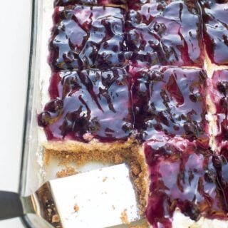 Sliced blueberry cheesecake squares in a rectangular pan, with a square missing.