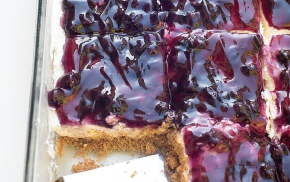 Sliced blueberry cheesecake squares in a rectangular pan, with a square missing.