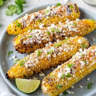 Elote grilled corn on a blue plate with a lime wedge.