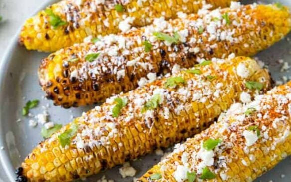 Elote grilled corn on a blue plate with a lime wedge.