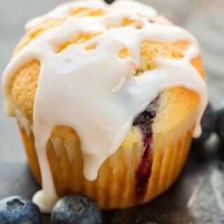 A lemon blueberry muffin topped with glaze, next to fresh blueberries.