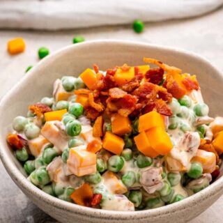 A bowl of creamy pea salad topped with bacon.