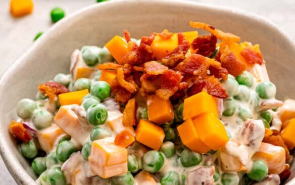 A bowl of creamy pea salad topped with bacon.