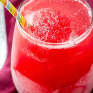 A glass of bright red rhubarb slush with a straw.