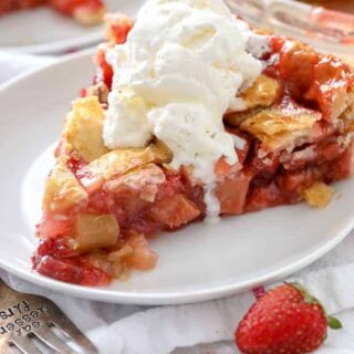A slice of strawberry rhubarb pie on a plate topped with whipped cream.