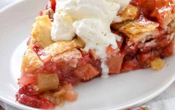 A slice of strawberry rhubarb pie on a plate topped with whipped cream.