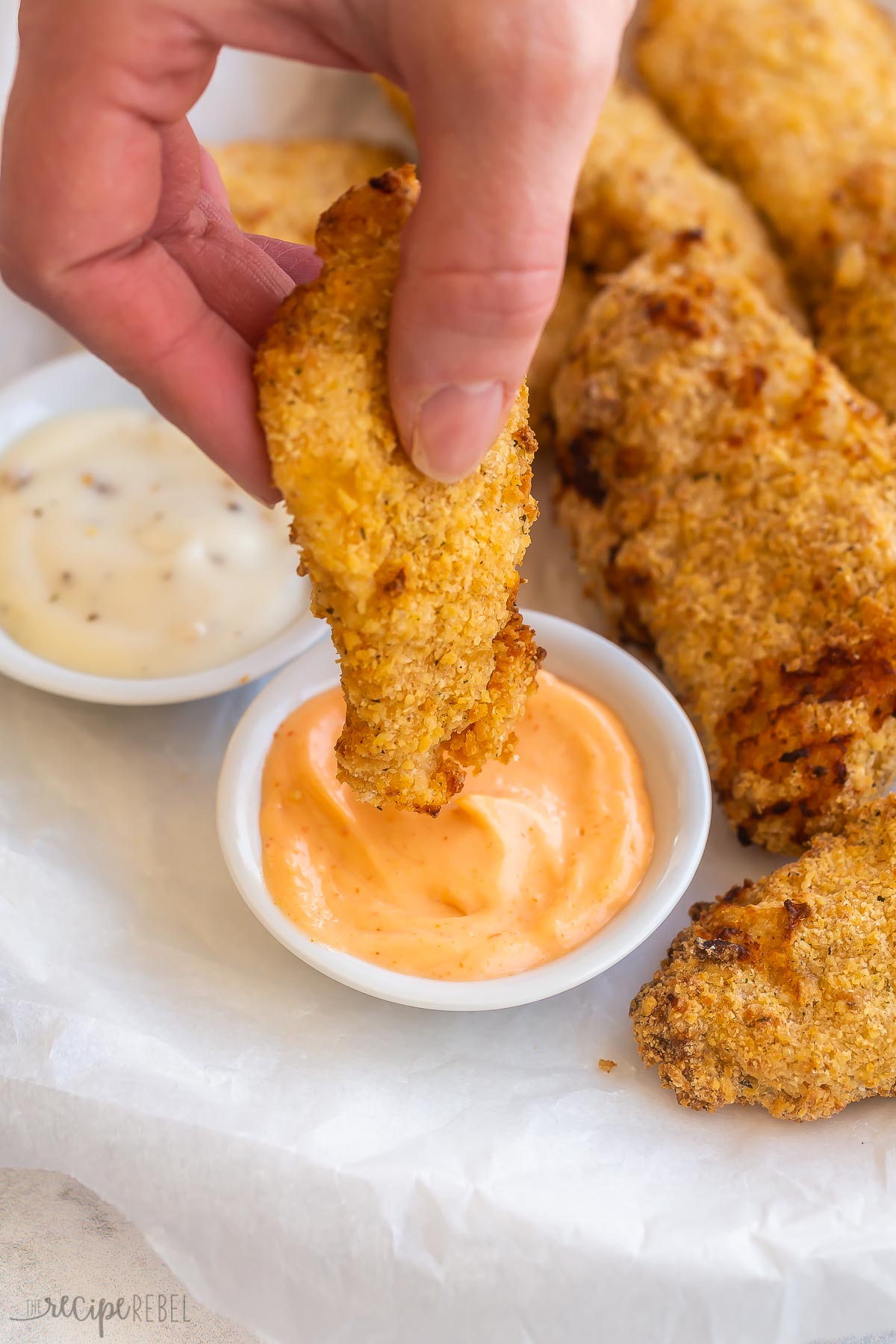hand dipping air fryer chicken tender into spicy mayo
