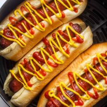 close up image of air fryer hot dogs in air fryer basket with ketchup and mustard